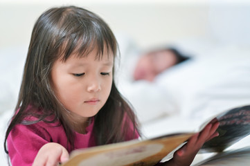 Asian little girl reading a tale book on bed before sleep in the bedroom