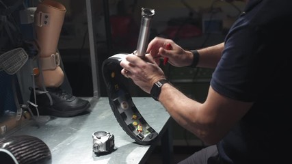 Production of a prosthetic leg. A man creates part of the leg. An engineer is testing the mechanical joint of a prosthetic leg. New sports body part. - Powered by Adobe