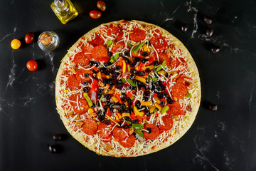 Extra large pizza with olives and tomatoes on black background.