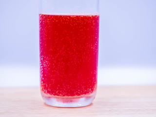 Closeup of sparkling fizzy bubbles in a glass of cold multivitamin water dissolved from effervescent tablet pills on wooden table and gray blurry bedroom or living room background.