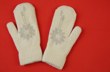 White wool mittens with rhinestone snowflake isolated on a red background with copy space. Flat lay, top view. The concept of winter clothing and accessories Winter background, banner, pattern, card.