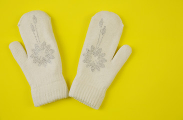 White wool mittens with rhinestone snowflake isolated on a yellow background. Copy space. Flat lay, top view. The concept of winter clothing and accessories Winter background, banner, pattern, card.