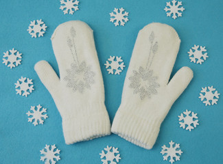 White wool mittens with rhinestone snowflake isolated on a blue background with snowflake. The concept of winter clothing and accessories. Winter background. Flat lay. Top view.