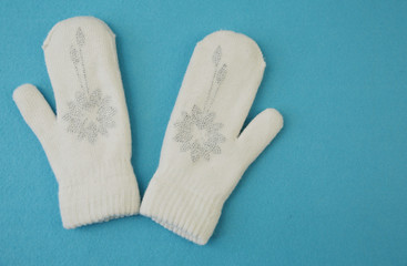 White wool mittens with rhinestone snowflake isolated on a blue background with copy space. flat lay, top view. The concept of winter clothing and accessories. Background, banner, pattern, card.