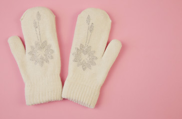 White wool mittens with rhinestone snowflake isolated on a pink background with copy space. flat lay, top view. The concept of winter clothing and accessories Winter background, banner, pattern, card.