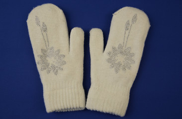 White wool mittens with rhinestone snowflake isolated on a blue background. flat lay, top view. The concept of winter clothing and accessories Winter background. 