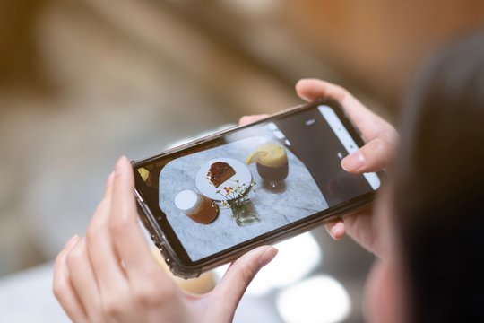 A girl take a picture of coffee and cake by smartphone in cafe