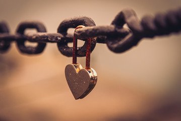A romantic closed and rusty heart shaped padlock hanging from a chain beside a river with blurred...