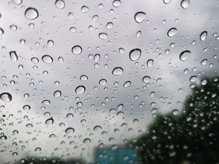 Selective focus of Rain drops on window glasses surface with dark cloudy background , rainy season,