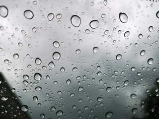 Selective focus of Rain drops on window glasses surface with dark cloudy background , rainy season,