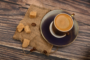 A Cup of coffee and pieces of brown sugar on a wooden background.