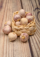 A few heads of young garlic in a wicker basket on a wooden background. Autumn harvest. Modern agriculture. Close up.