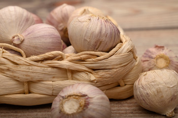 A few heads of young garlic in a wicker basket on a wooden background. Autumn harvest. Modern agriculture. Close up.
