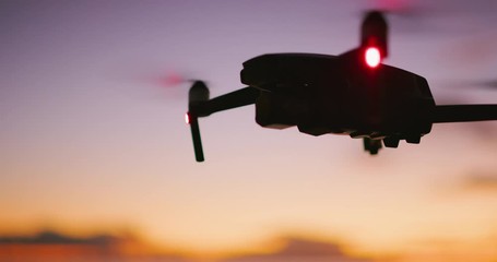 Close up view of a quadcopter drone silhouette hovering and flying at sunset with a purple yellow sky - Powered by Adobe