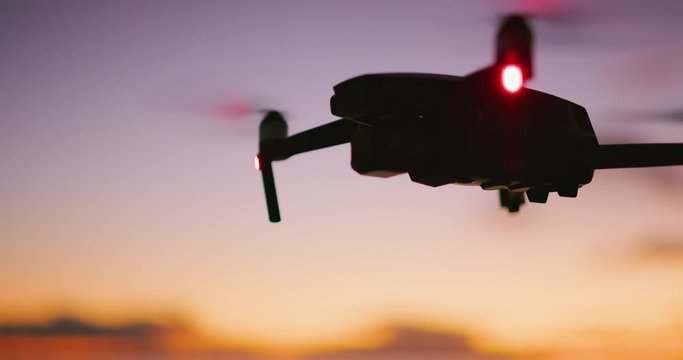 Close up view of a quadcopter drone silhouette hovering and flying at sunset with a purple yellow sky