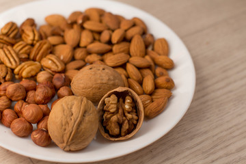 walnuts, almonds, pecans and hazelnuts on a white plate on a woodden table