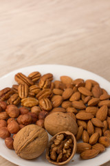 walnuts, almonds, pecans and hazelnuts on a white plate on a woodden table