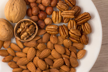 walnuts, almonds, pecans and hazelnuts on a white plate on a woodden table