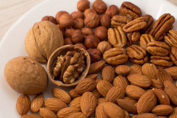 walnuts, almonds, pecans and hazelnuts on a white plate on a woodden table