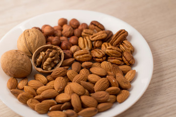 walnuts, almonds, pecans and hazelnuts on a white plate on a woodden table