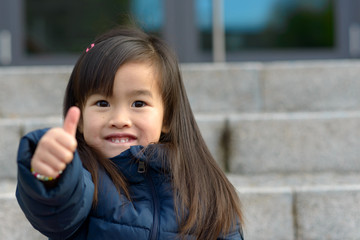 Vivacious little girl giving a thumbs up gesture