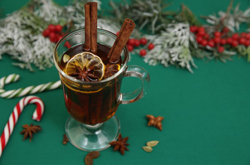 mulled wine a hot drink or tea with spices and caramel sugar cane, spruce branch and red berries on a green background. Isolated. Traditional winter drink. Christmas concept, background, composition