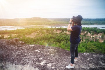 Young tourist asian woman wearing black hat taking photo landscape view on the top of mountain hills with tropical nature background in thailand , summer vacation holiday concept.