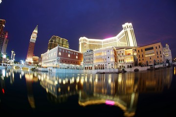 Night scenery of the extravagant exterior of  luxury hotels & casino resorts in Macau, China, with reflections of beautiful buildings and colorful neon lights in the water of a pool