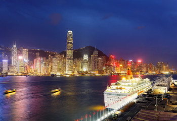 Night skyline of Hong Kong, with landmark IFC Tower standing amid skyscrapers by Victoria Harbour, a luxury cruise liner parking at Ocean Terminal in Tsim Sha Tsui and city lights glowing in blue dusk