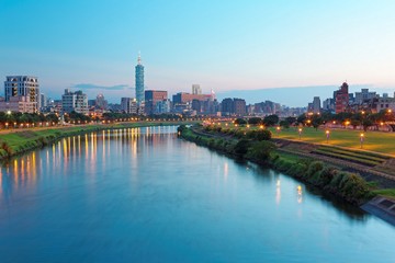 Obraz na płótnie Canvas Beautiful riverside scenery of busy Taipei City with view Taipei landmark Tower, Keelung River and downtown area at dusk ~ A Blue and Gloomy evening in Taipei