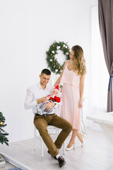 A young beautiful friendly family with a small child in a little Santa costume celebrate Christmas and New Year in their home in a bright living room