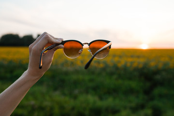 sunglasses in hand. Sunglasses. Sunset on the field. look through the sunglasses at sunset. holds sunglasses