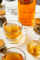 Cup of hot black tea on white table with dry tea jar