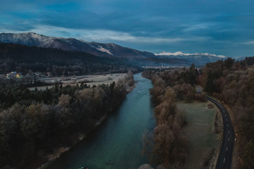 Aerial drone shot of a river, road and forest covered in frost on a misty foggy morning. View towards the mountains, famous mount Triglav in Slovenia in the middle.