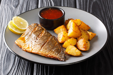 Grilled dorado (sea bream) fillet with potato wedges and sauces close-up on a plate on the table. horizontal