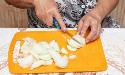 The hostess cuts the onion with a knife on the board