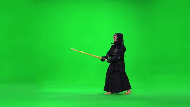 Masculine Kendo warrior practicing martial art with the bamboo bokken on green screen.