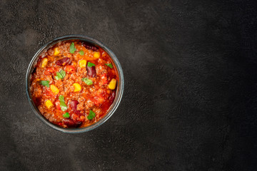 Chili con carne, Mexican stew with beans, ground meat, corn, and chili peppers, top shot on a black background with copy space