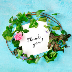 Thank you card with a wreath of ivy with vibrant green leaves and a rose flower, top shot on a blue...