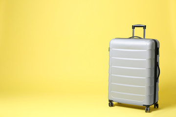 Stylish grey suitcase on yellow background. Space for text