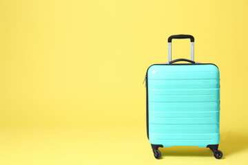 Stylish turquoise suitcase on yellow background. Space for text