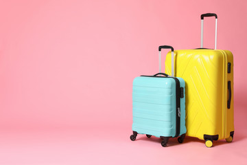 Stylish yellow and turquoise suitcases on pink background. Space for text