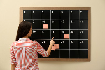 Young woman near board calendar  indoors, back view
