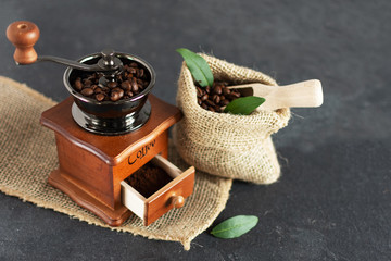 Manual vintage coffee grinder and coffee beans in a burlap bag on a wooden table.