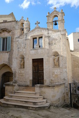 Fototapeta na wymiar Church of San Biagio in Matera located in the Foggiali area. The construction is made of blocks of tufa stone of beige color. Facade with two small bells.