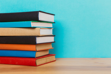 A simple composition of many hardback books, raw books on a wooden table and a bright blue background