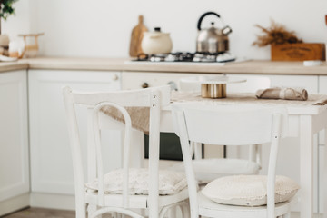 Modern new bright kitchen interior with white furniture and a dining table. gas stove with kettle and pan