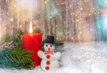 Burning red candle with a little snowman in the snow, copy space