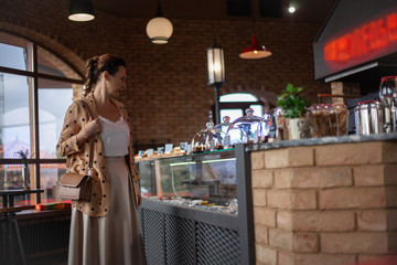 Matured middle aged woman dressed style fasnion clothes chooses the pastry bakery on showcase table in cafe.