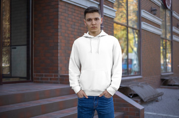 Fototapeta premium Template male white hoodie on a guy, front view, presentation of clothes on the street.